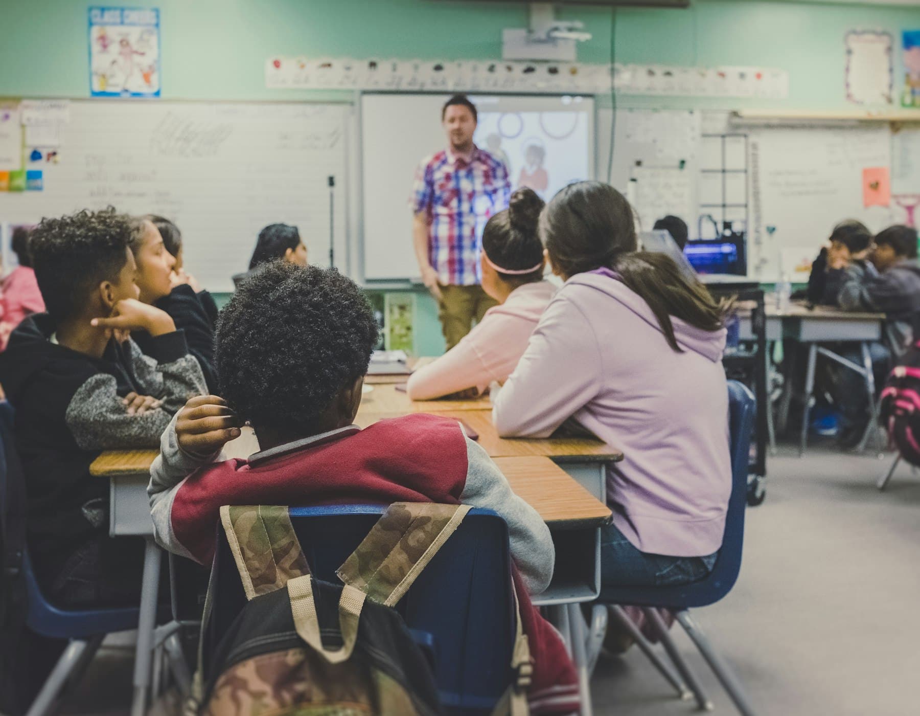 Students seated in a classroom, listening to a teacher.