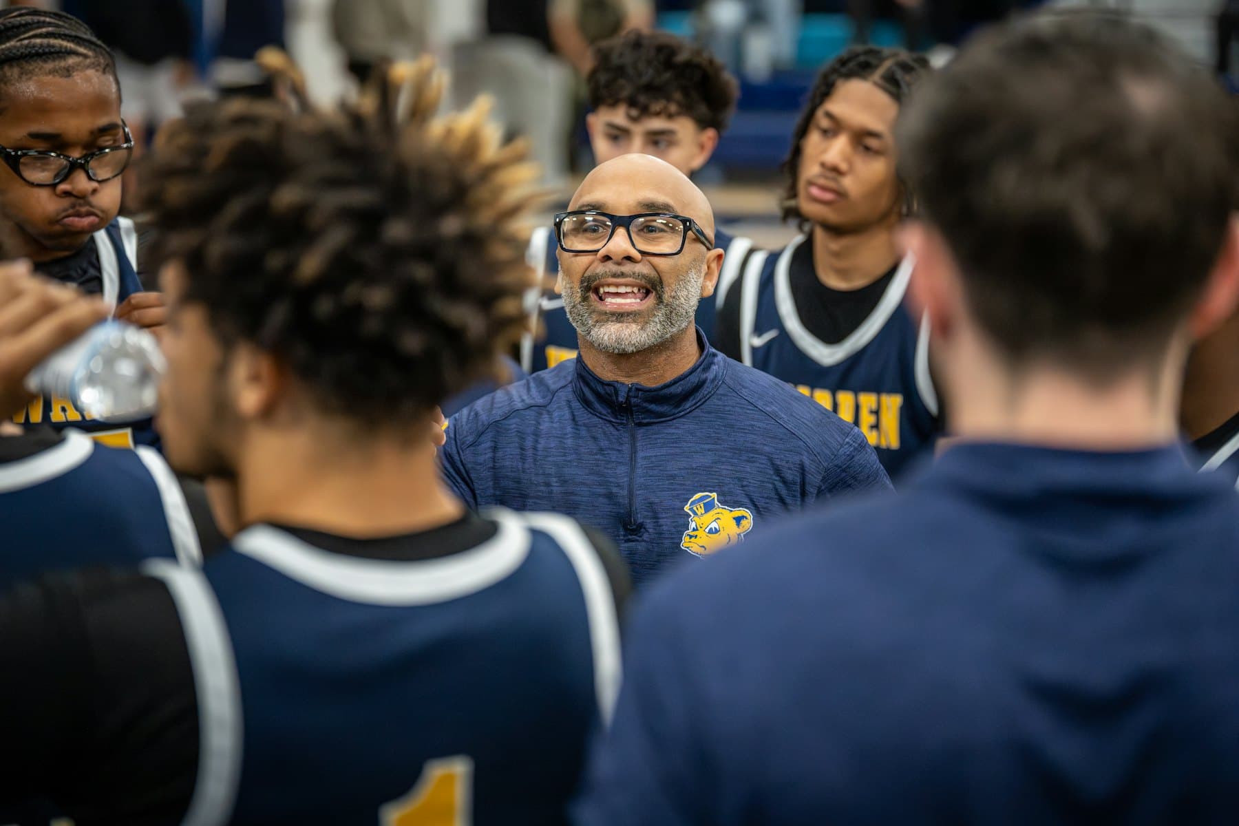 A coach talking with young players gathered in a close circle.
