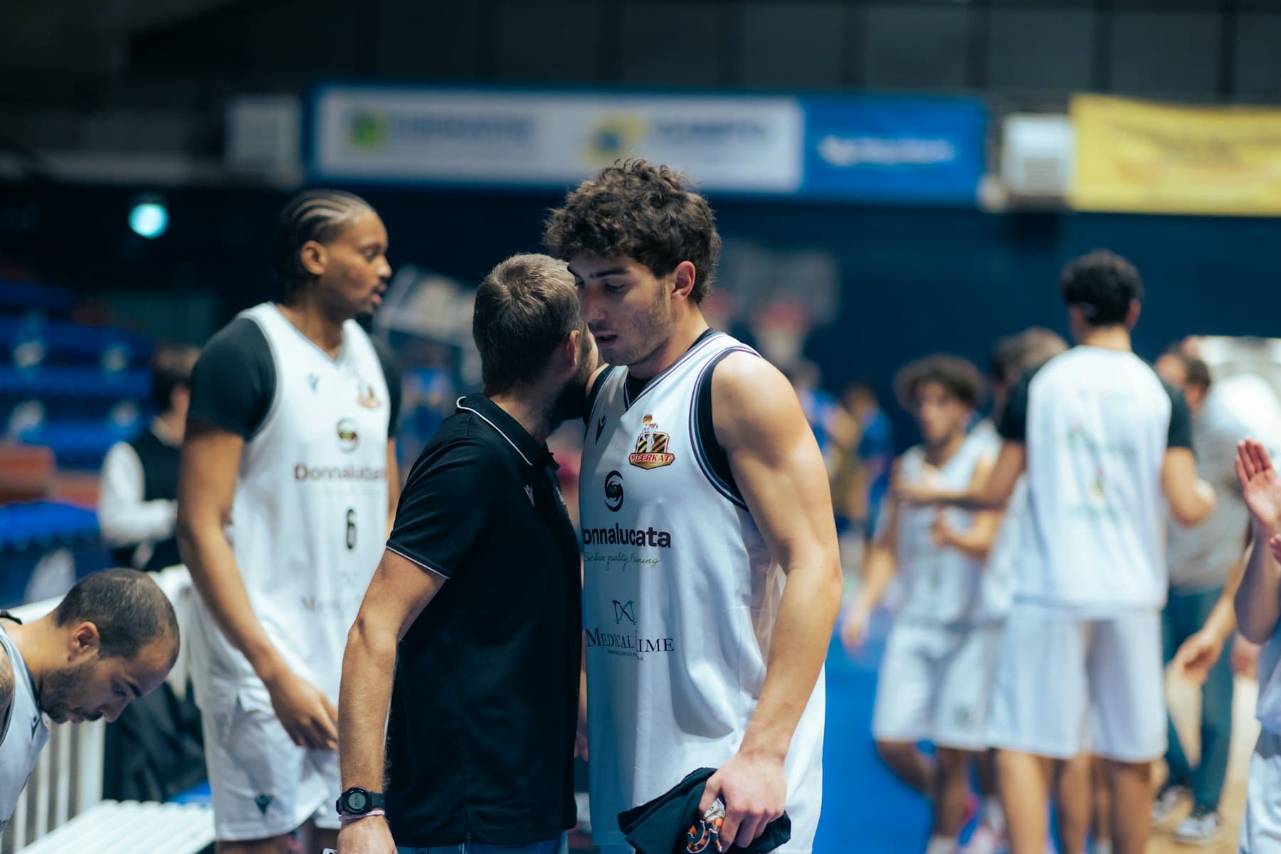A coach speaking closely with a basketball player at courtside.